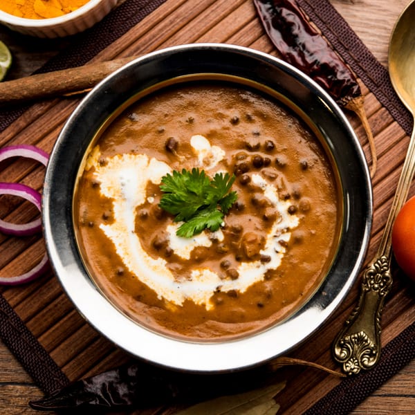 A bowl of creamy Dal Makhani, garnished with fresh cilantro and a swirl of cream, on a wooden surface.