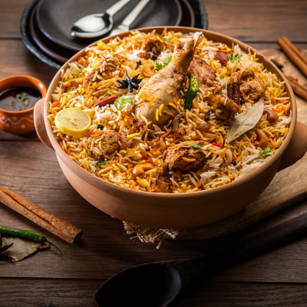 A large clay pot filled with chicken biryani, garnished with lemon, spices, and herbs.