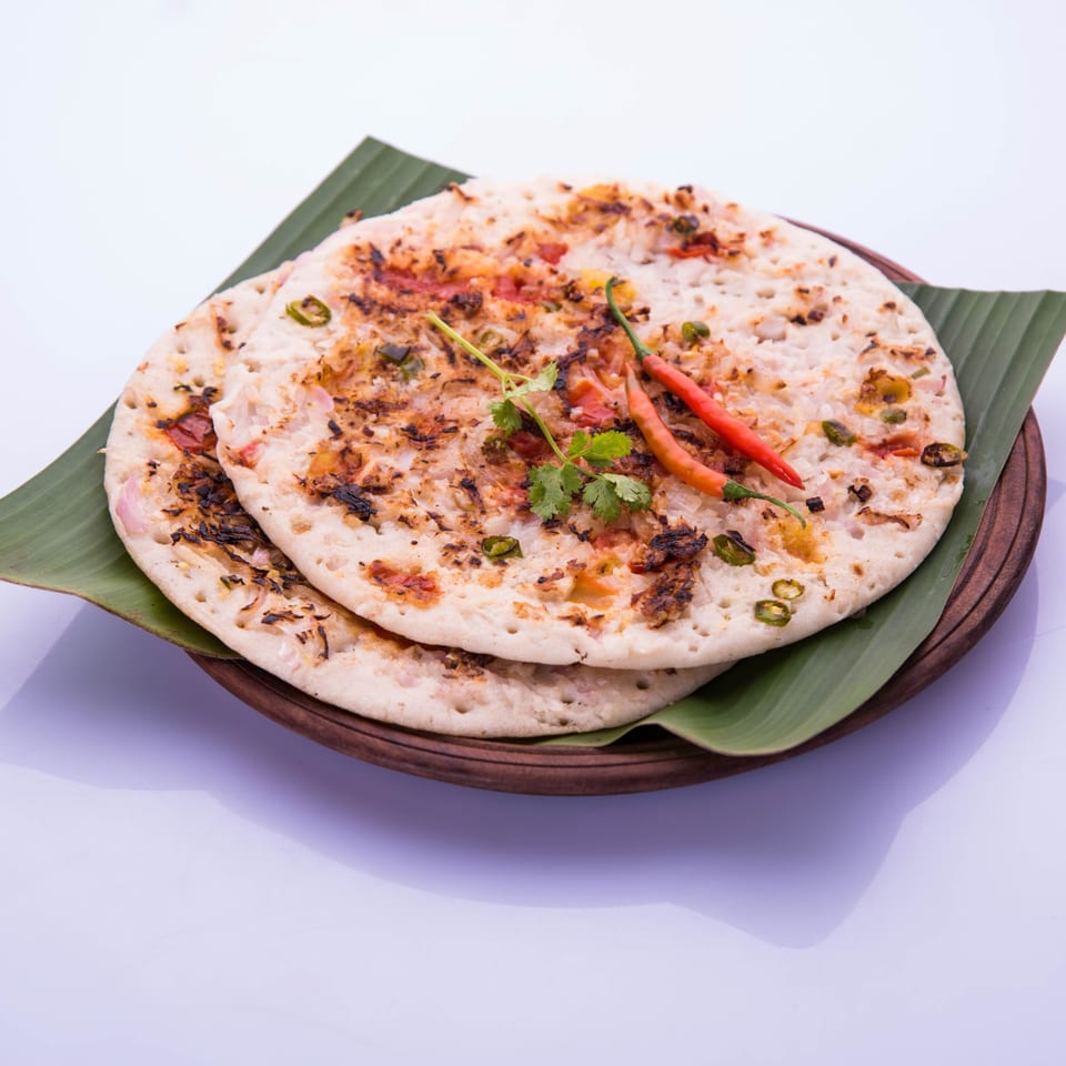 Two uttapam pancakes, garnished with cilantro and red chilies, on a banana leaf.