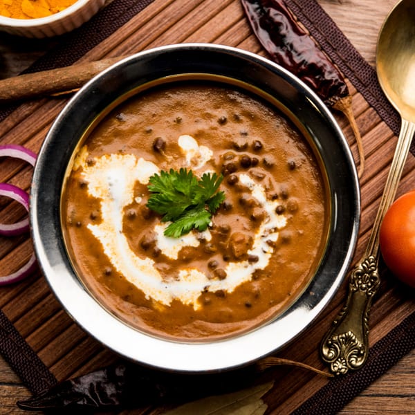 A bowl of creamy Dal Makhani, garnished with fresh cilantro and a swirl of cream, on a wooden mat.