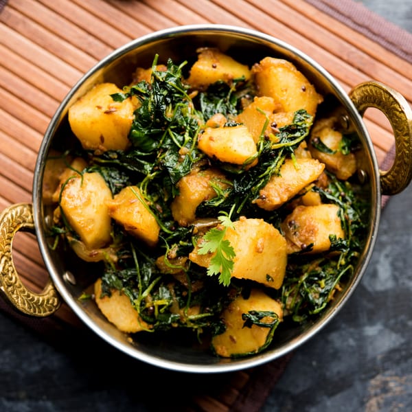 A close-up of a golden bowl filled with Indian aloo methi, featuring potatoes and fenugreek leaves.