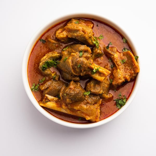 Overhead view of a white bowl filled with rich, red Indian mutton curry garnished with fresh cilantro.