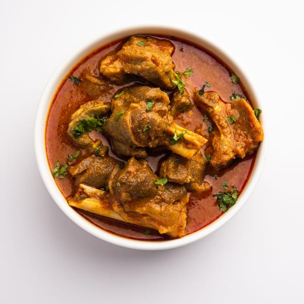 Mutton curry, a rich red stew with tender meat pieces and fresh cilantro, served in a white bowl.