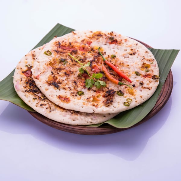 Two savory uttapam pancakes, garnished with red chilies and cilantro, on a banana leaf.