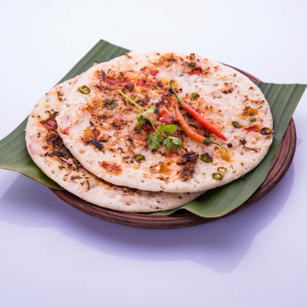 Two savory uttapam pancakes with vegetables, chili, and cilantro on banana leaves.