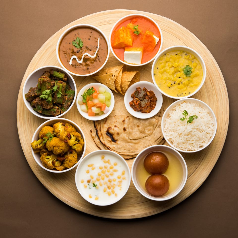 A wooden platter filled with various Indian dishes, including curries, rice, flatbread, and desserts.