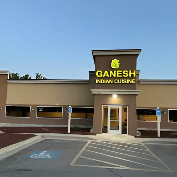 Exterior of Ganesh Indian Cuisine restaurant with a brown facade, yellow sign, and parking lot.
