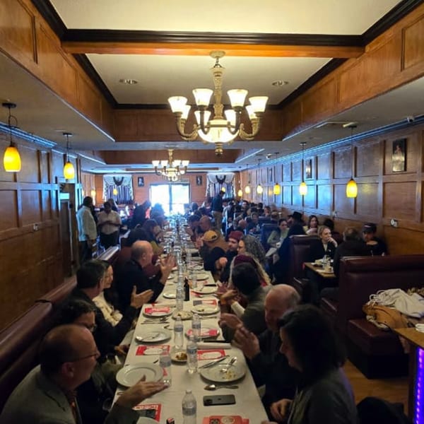 A long dining room with many people seated at a banquet table and in booths.