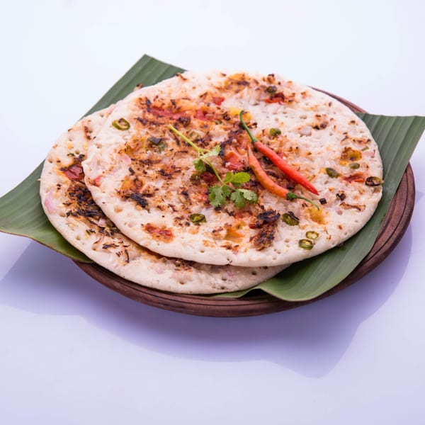 Two savory uttapam pancakes, garnished with red chilies and cilantro, on a banana leaf.
