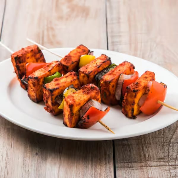 Three paneer tikka skewers with red and green peppers, and onions on a white plate.