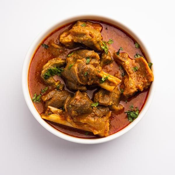 Mutton curry, a rich red stew with tender meat pieces and fresh cilantro, in a white bowl.