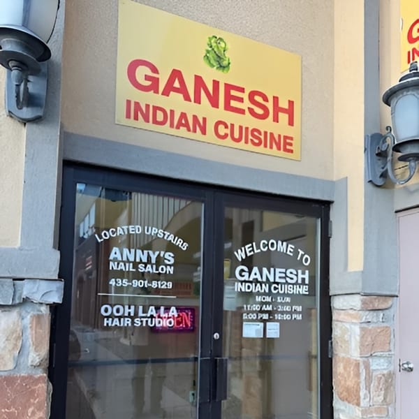The exterior of Ganesh Indian Cuisine, with its sign and glass entrance doors displaying hours and other businesses.